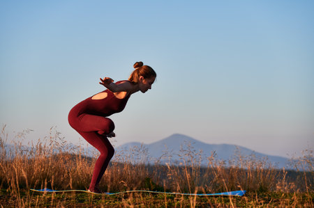 Sporty girl doing difficult yoga position. Practicing yoga at dawn. Young woman exercising outdoor on background of mountains.の写真素材