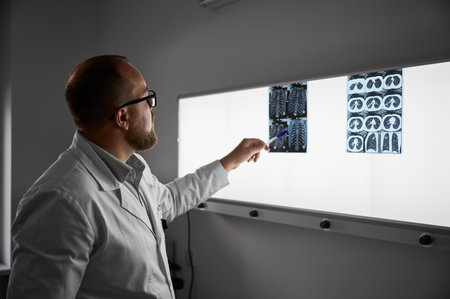 Side view of doctor studying MRI results. Male specialist working in clinic, carrying out description of the radiographs of a patient, pointing by pen. Concept of medicine and healthcare.の写真素材