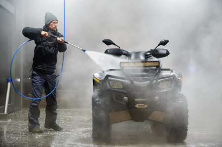Full length of man washing all-terrain vehicle with high pressure water sprayer auto washerの写真素材