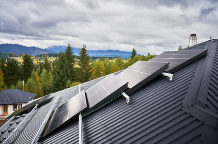 Solar photovoltaic panels on a roof of house. Dark blue solar cells prepared for installation, lying on rooftop of modern cottage on background of mountains. Green alternative energy concept.の写真素材
