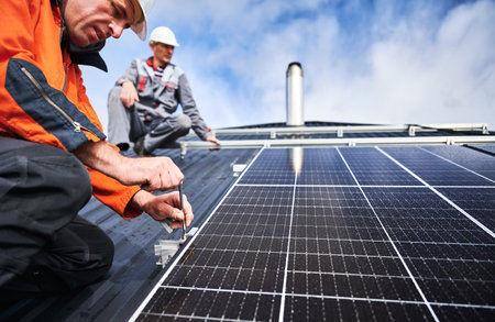 Workers installing photovoltaic solar panels on roof of house. Men engineers in helmets building solar module system with help of hex key. Concept of alternative, renewable energy.の写真素材