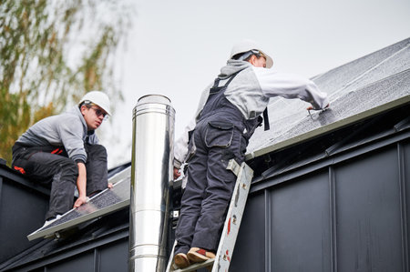 Installers installing photovoltaic solar panels on roof of house. Men engineers in helmets building solar module system with help of hex key. Concept of alternative, renewable energy.の写真素材
