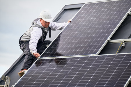 Technician mounting photovoltaic solar panels on roof of house. Man engineer in helmet installing...