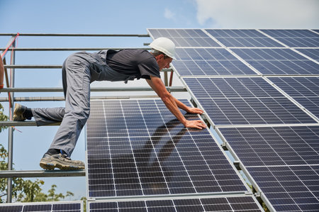 Male worker buildingg photovoltaic solar panel system outdoors. Man electrician placing solar module on metal rails, wearing construction helmets. Renewable and ecological energy.の写真素材