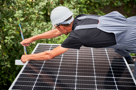 Man installer mounting photovoltaic solar moduls on roof of house. Electrician in helmet installing solar panel system outdoors, tightening with hex key. Concept of alternative and renewable energy.の写真素材