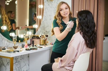 Female makeup artist applying pencil eyeliner to client upper eyelid. Beauty specialist in sterile gloves doing professional eye makeup on woman in beauty salon.の写真素材