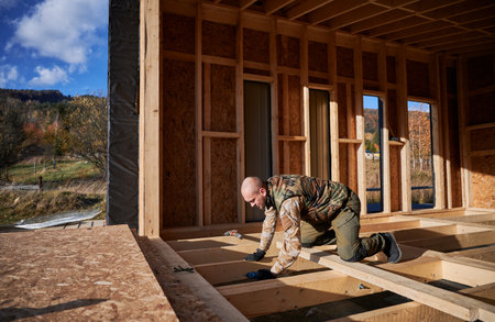 Male builder working with screwdriver inside of future cottage. Man worker building wooden frame house in the Scandinavian style barnhouse. Carpentry and construction concept.の写真素材