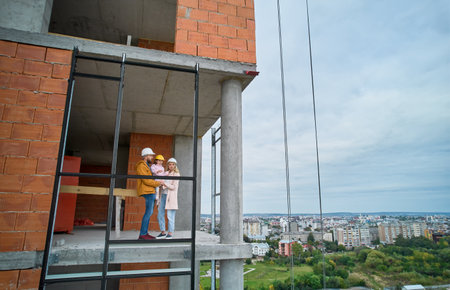 Man with wife and child standing inside residential building under construction. Urban district with newly constructed apartment building and family new residents real estate buyers. Drone viewの写真素材