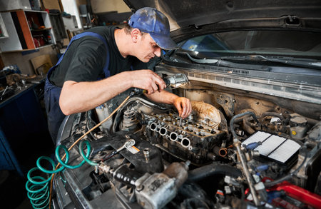 Man worker fixing car engine, working in garage, workshop, servicing center. Repairman, mechanic opening hood of car, examining.の写真素材