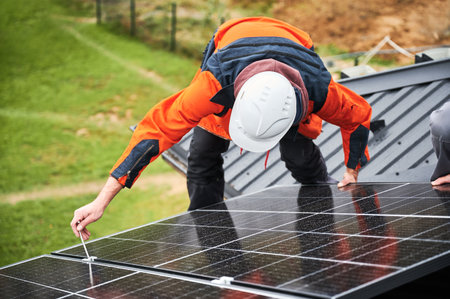 Builders installing photovoltaic solar panels on roof of house. Men engineers in helmets building solar module system with help of hex key. Concept of alternative, renewable energy.の写真素材