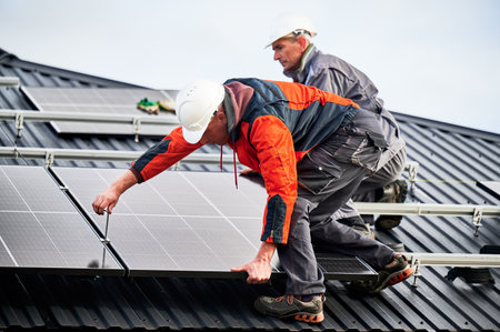 Builders installing photovoltaic solar panels on roof of house. Men engineers in helmets building solar module system with help of hex key. Concept of alternative, renewable energy.の写真素材
