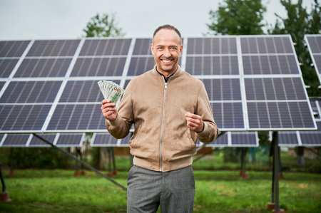 Man smiling with his earnings in hands. Young man happy about his profit from solar panels. Alternative energy and investment concept.の写真素材