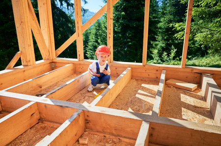 Young lad, the son of a carpenter, frolics amidst the construction of a wooden-framed house. Concept of early development and mutual assistanceの写真素材