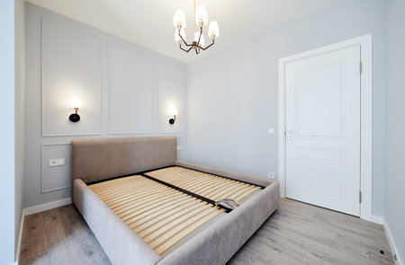 Bedroom with large bed, laminate floor, white walls, closed door and lamps in apartment after renovation. Interior of modern apartment with elegant minimalist design and comfortable sofa bed.の写真素材