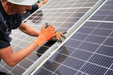 Close up of man solar installer mounting photovoltaic solar panel outdoors. Male technician in safety construction helmet assembling solar modules. Concept of alternative energy sources.の写真素材