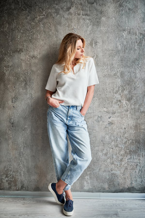 Full length of woman in casual clothes standing by the wall in new apartment. Female person keeping hands in jeans pockets..の写真素材