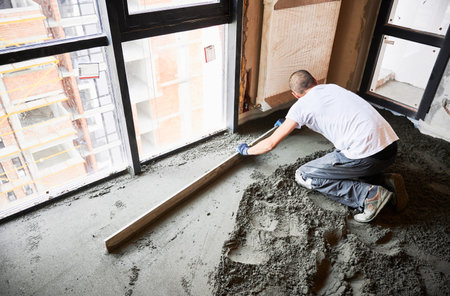 Man flattening and smoothing surface with straight edge in apartment during renovation. Male construction worker using screed rail while screeding floor in living room.の写真素材