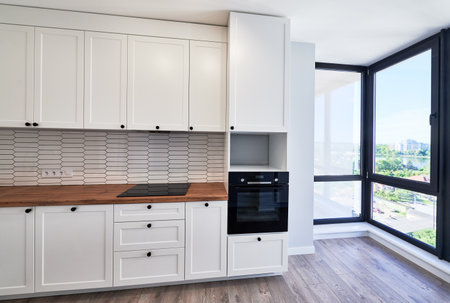 Kitchen with laminate floor, white walls, doorway and modern kitchen set with electric stove, counter, sink and oven. Apartment kitchen room with elegant minimalist design in white colors.の写真素材