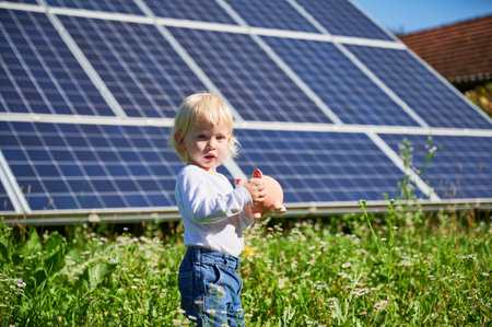 Little cute boy saving money in piggy bank. Small kid learning about saving money for future. Blond child holding piggy bank on background of solar panels at sunny day.の写真素材