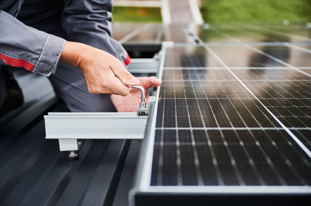 Professional installation of PV system on a roof. Close up view of competent engineer securing photovoltaic solar cell. Adjusting solar panel on top of house.の写真素材