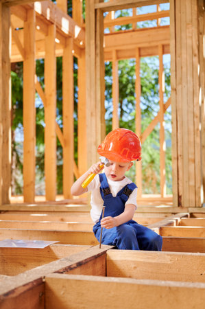 Boy, offspring of skilled artisan, revels in playful construction of timber-framed house. Child learning the art of driving nails into the wood with hammer. Concept of early childhood development.の写真素材