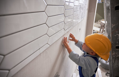 Little child construction worker installing ceramic tile on the wall in apartment under renovation....