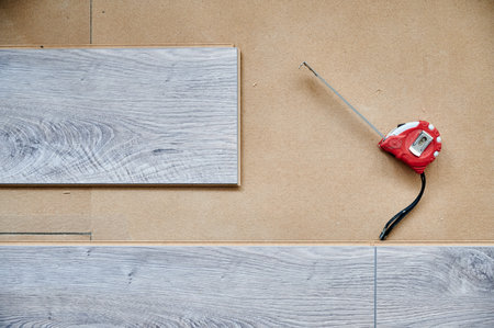 Tape measure and wooden flooring planks for home renovation, construction works and interior design. Measuring tape ruler tool and laminate boards with pattern and wood texture for flooring.の写真素材