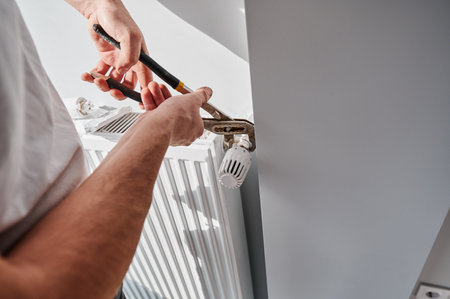 Close up of man using wrench tool while installing heating radiator in apartment under renovation. Male plumber working on heating system installation. Home renovation and plumbing works concept.の写真素材