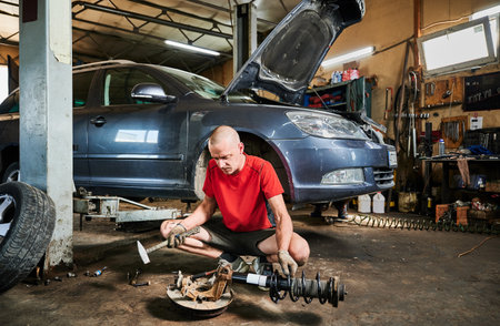 Repairman, worker fixing car, holding hammer, looking. Hardworking man working in garage, servicing auto center, repairing automobile. Concept of manal men work.の写真素材