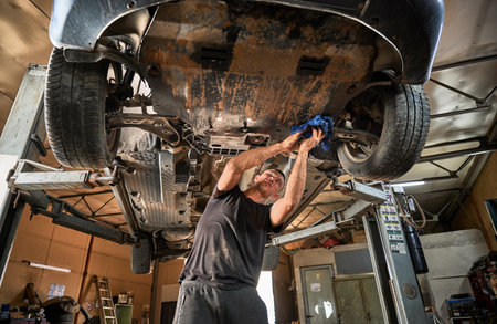 Repairman, worker repairing car, holding rag, wiping. Strong, hardworking man working in servicing center, mainteining automobiles. Concept of manual labor.の写真素材