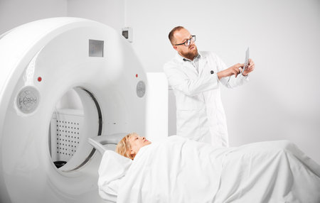 Medical computed tomography or MRI scanner. Doctor holding and explaining results of MRI. Woman patient lying on CT scan bed. Concept of medicine, healthcare and modern diagnostics.の写真素材