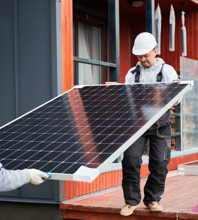 Engineers installing solar panel system. Men workers in helmets carrying photovoltaic solar module...