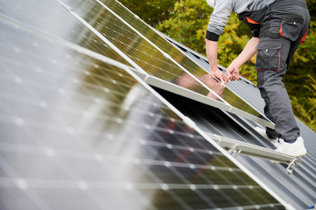 Man technician mounting photovoltaic solar panels on roof of house. Close up view of engineer installing solar module system with help of hex key. Concept of alternative, renewable energy.の写真素材