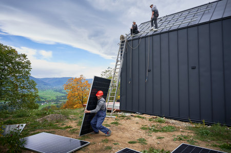 Technician building solar panel system on roof of house. Man worker in helmet carrying photovoltaic solar module outdoors. Concept of alternative and renewable energy.の写真素材
