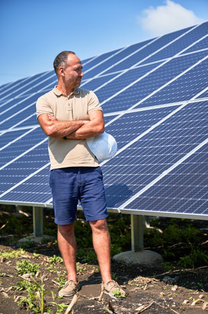 Professional worker glad about work he did. Installed PV panel ready to work. Adult male looking at solar panel with crossed arms.の写真素材