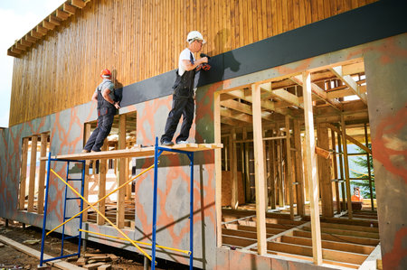 Carpenters constructing wooden framed house. Two men workers cladding facade of house with cement particle boards, fastening them with screwdrivers. Concept of modern eco-friendly construction.の写真素材