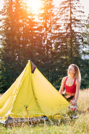 Woman hiker camping in mountains. Young female tourist putting tent, wearing sportswear, traveling. Concept of tourism and adventure.の写真素材