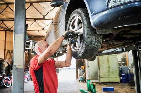 Mechanic, worker, repairman changing wheels of car in garage. Man wearing dirty gloves, working in servicing center, repairing cars. Concept of manual labor.の写真素材