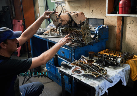 Side view of repairman, worker wearing cap, working in garage, workshop. Engineer, mechanic repairing, fixing car, holding steel equipment by hands. Concept of manual labor.の写真素材