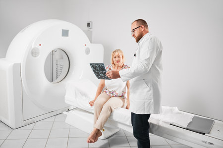 Medical computed tomography or MRI scanner. Doctor holding and explaining results of MRI. Woman patient after MRI, sitting on couchette. Concept of medicine, healthcare and modern diagnostics.の写真素材