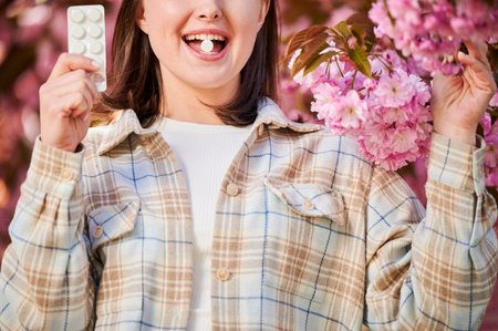 Woman allergic suffering from seasonal allergy at spring. Cropped view of young woman applying allergy pill, posing in blossoming garden at springtime. Antihistamine medication conceptの写真素材