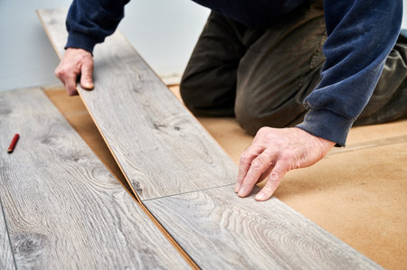 Close up of man construction worker installing laminate timber flooring in apartment under renovation. Male hands placing laminate planks on the floor at home. Flooring renovation concept.の写真素材