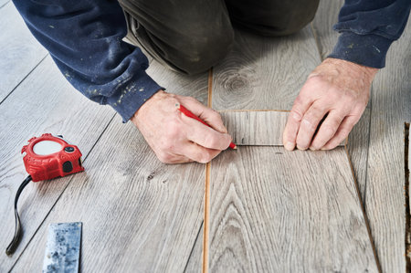 Close up of man construction worker with pencil in hand drawing line on laminate timber board. Male worker preparing laminate material for floor installation at home during renovation.の写真素材