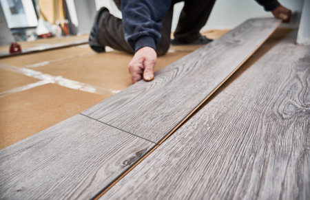 Close up of man construction worker installing laminate timber flooring in apartment under renovation. Male hands placing laminate planks on the floor at home. Flooring renovation concept.の写真素材
