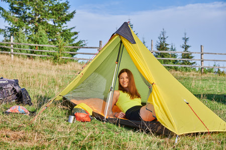 Woman traveller camping outdoors. Female tourist traveling, hiking in mountains. Attractive, sporty woman sitting in tent, having break, looking at camera. Concept of tourism and adventure.の写真素材