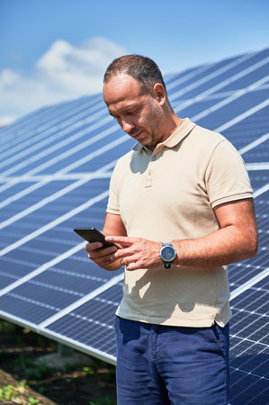 Busy businessman trying to keep up with everything. Confident man checking his new investment. Young man looking at his mobile phone on background of solar panel.の写真素材