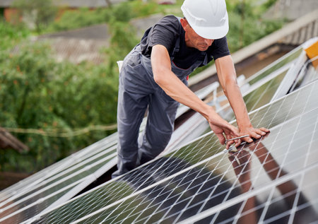 Man installer installing photovoltaic solar moduls on roof of house. Electrician in helmet building solar panel system outdoors with help of hex key. Concept of alternative and renewable energy.の写真素材