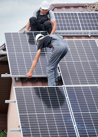 Men technicians mounting photovoltaic solar moduls on roof of house. Electricians in helmets installing solar panel system outdoors. Concept of alternative and renewable energy.の写真素材