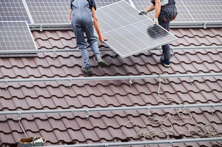 Men technicians carrying photovoltaic solar moduls on roof of house. Cropped view of engineers building solar panel system outdoors. Concept of alternative and renewable energy.の写真素材
