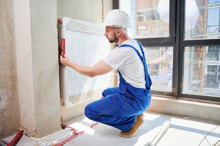 Male worker using spirit level tool while installing heating system at home. Man plumber measuring radiator pipes level with building instrument in apartment under renovation.の写真素材